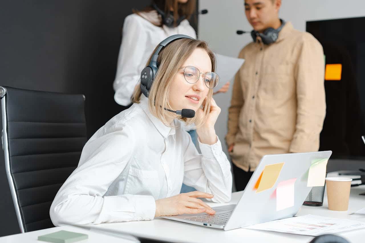 A woman with headphones sits at a desk, focused on her laptop while working or studying.