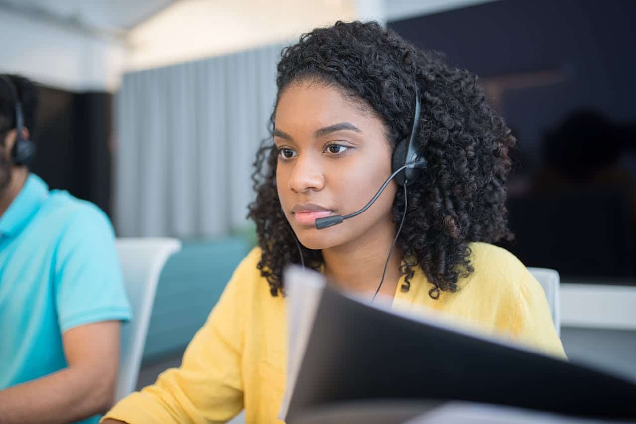 A young woman with a headset focused on her computer screen while working in a modern office environment.